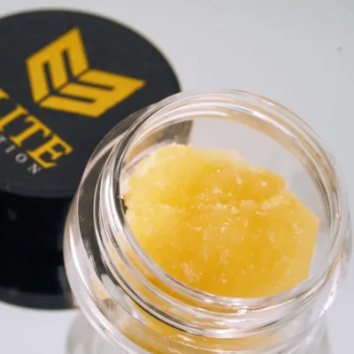 Yellow cannabis live resin concentrate biscotti strain in a clear glass jar with black Elite Elevation lid in background